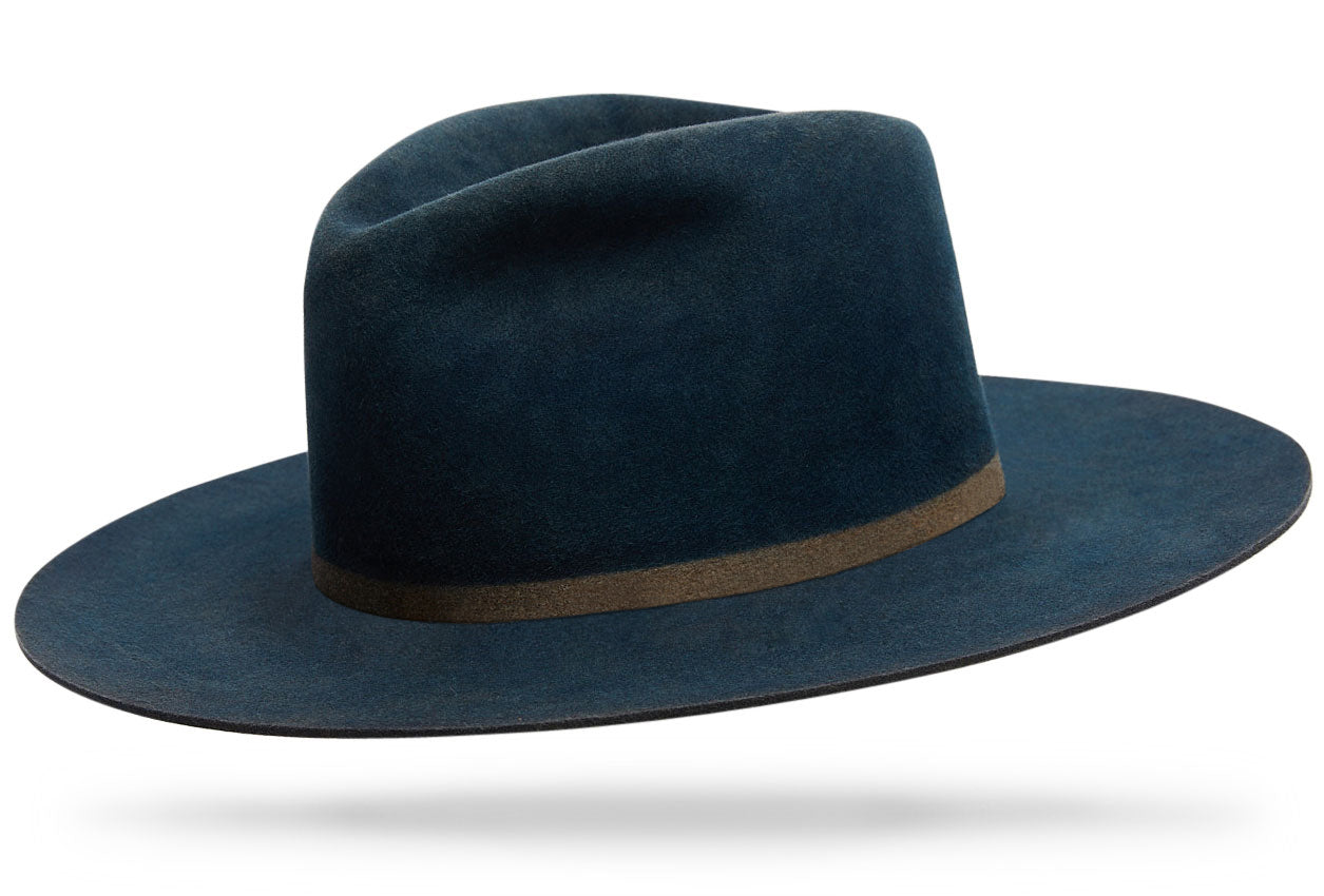 Design
Our classic Ash proportions, reimagined in a softer, packable beaver felt. Designed to fold, travel, and reshape beautifully, each piece is hand-dyed in our studio using layered techniques that give the Blue Ash tone its subtle depth and character.Crafted from dressed beaver fur felt and finished with a 4” teardrop crown and 3.5” straight brim, this is a versatile, resilient hat made to be worn often and live well over time.
*** The model is wearing the blue ash Western body version with similar proportions. 
Material
100% Dressed Beaver fur Felt Hat sustainably acquired with natural green pigments. Natural dyeing minimizes the harmful effects on the surrounding environment. Our custom hats are hand-dyed by using plants and vegetable-based pigments.
Specifications
- A 4 Tear Drop Crown with a 3 1/2 straight brim- Triple hand dyed- With an invisible band - Handcrafted in our atelier in NYC. - Please allow 6 weeks to custom make this special piece.