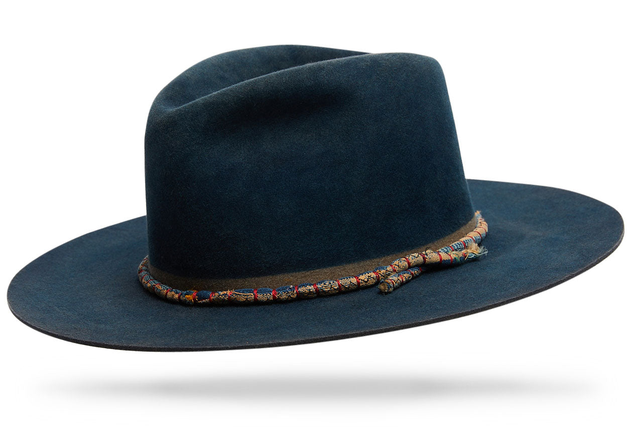 Design
100% Beaver Fur Felt triple hand-dyed indigo blue with different shades of blue from deep indigo blue to teal.  This 4 Tear Drop Crown with a 3 1/2' straight brim beauty comes with an invisible band and a hand-loomed vintage African cloth hand-rolled with red detailed thread.  A real workhorse, this Must-Have will last you a lifetime.
Material
100% Western Beaver fur Felt Hat sustainably acquired indigo dye treatment. Natural dyeing minimizes the harmful effects on the surrounding environment. Our custom hats are hand-dyed by using plants and vegetable-based pigments.
Specifications
A 4 Tear Drop Crown with a 3 1/2 straight brim with an admirable amount of strength and durability.  Handcrafted in our atelier in NYC. Please allow 6-8 weeks to custom make this special piece.